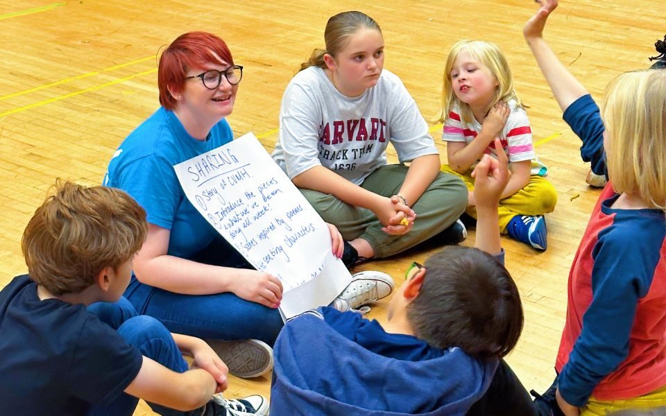 Imogen explains the upcoming performance to a group of young people, from a large sheet of paper. Credit: Aaron Cawood