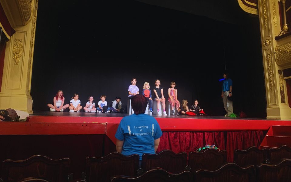 Young people stand and sit on the stage at City Varieties Music Hall, Imogen standing opposite them