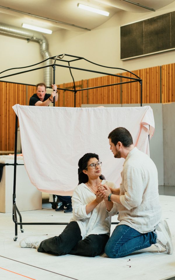 Isabelle Peters as Nanetta and Egor Zhuravskii as Fenton in rehearsal for Falstaff. They are holding hands and sitting on the ground. They are in front of a hanging sheet.
