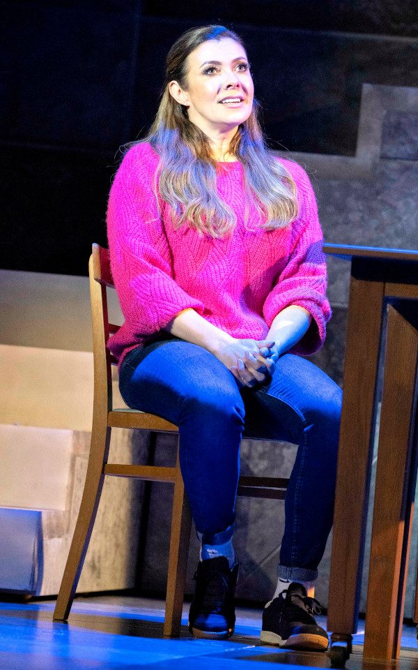 Kym Marsh is wearing a pink jumper and sitting on a chair.