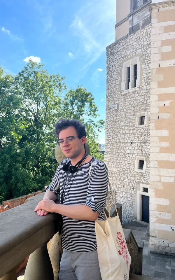 Dominick explores a building in the sun, resting on a wall and smiling to camera.