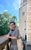 Dominick in their spare time. Dominick explores a building in the sun, resting on a wall and smiling to camera.