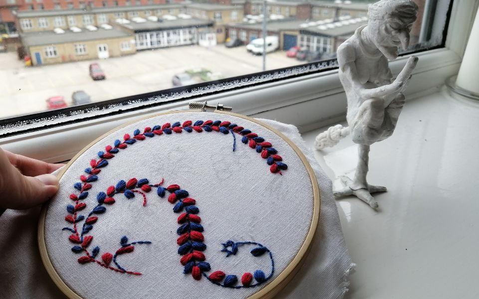 A piece of patterned embroidery and sculpture of a witch on a broom.