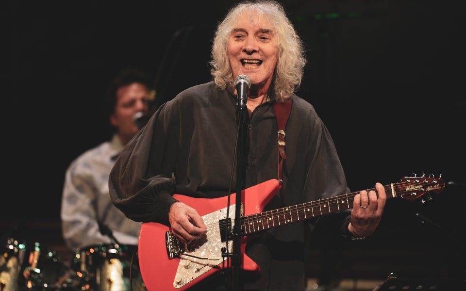 Albert Lee singing into a microphone while playing a red electric guitar