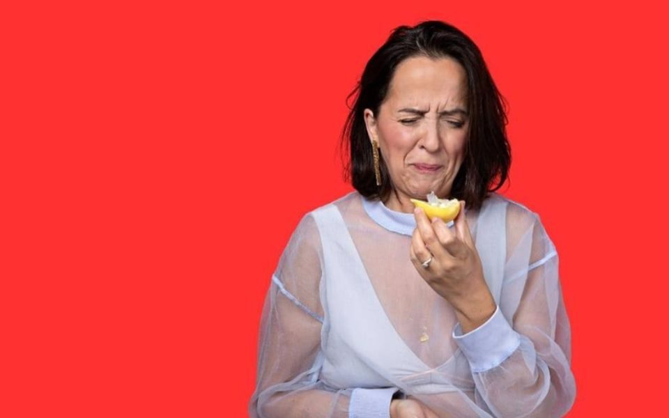 Luisa Omielan eating a lemon and pulling a face in front of a red background
