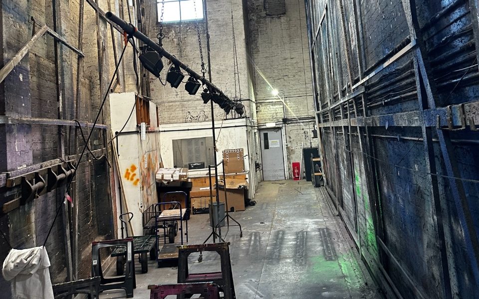 Backstage at Leeds Grand Theatre. There are paint splatters over the wall and stools laid out.