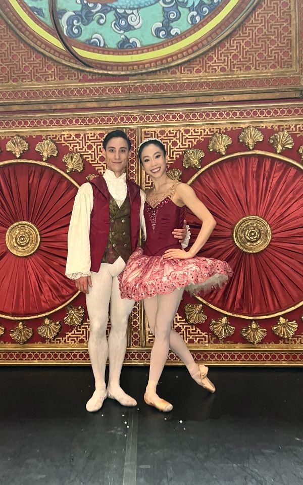 Sarah Chun and Kevin Peuong pose together in classical costumes, in front of a set-piece for Northern Ballet's The Nutcracker.
