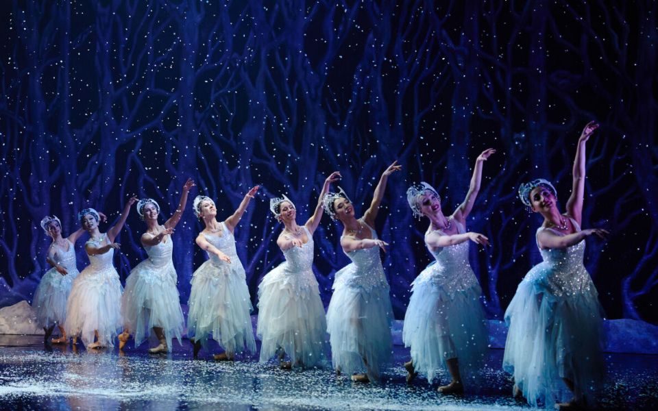A row of dancers pose together, arms outstretched against the backdrop of a forest.