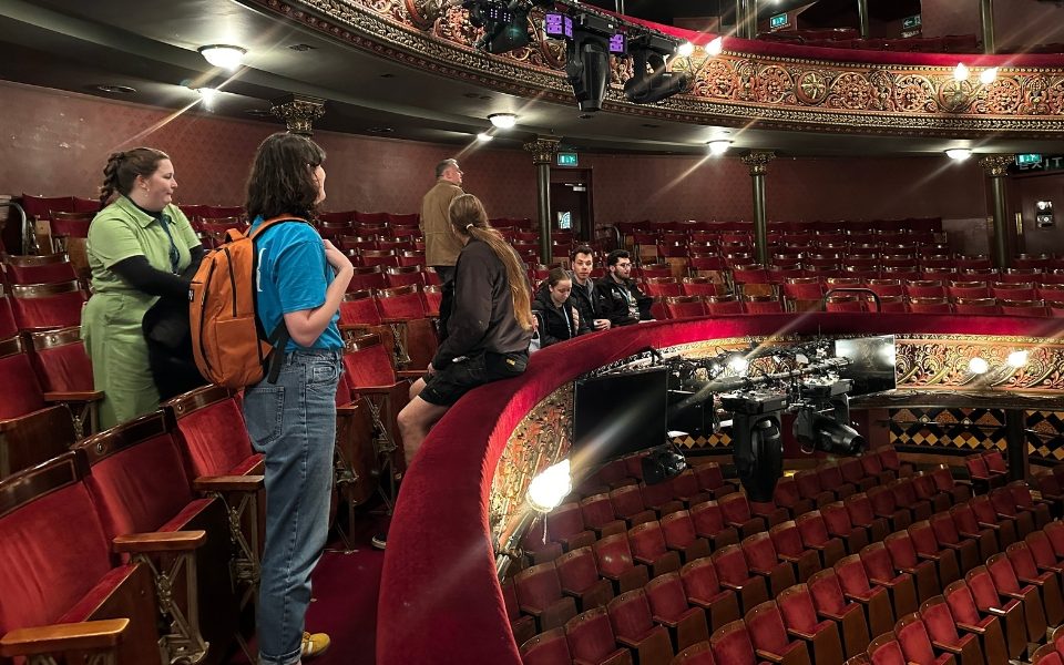 Students standing and sitting in chairs in the circle level of the Leeds Grand Theatre auditorium.