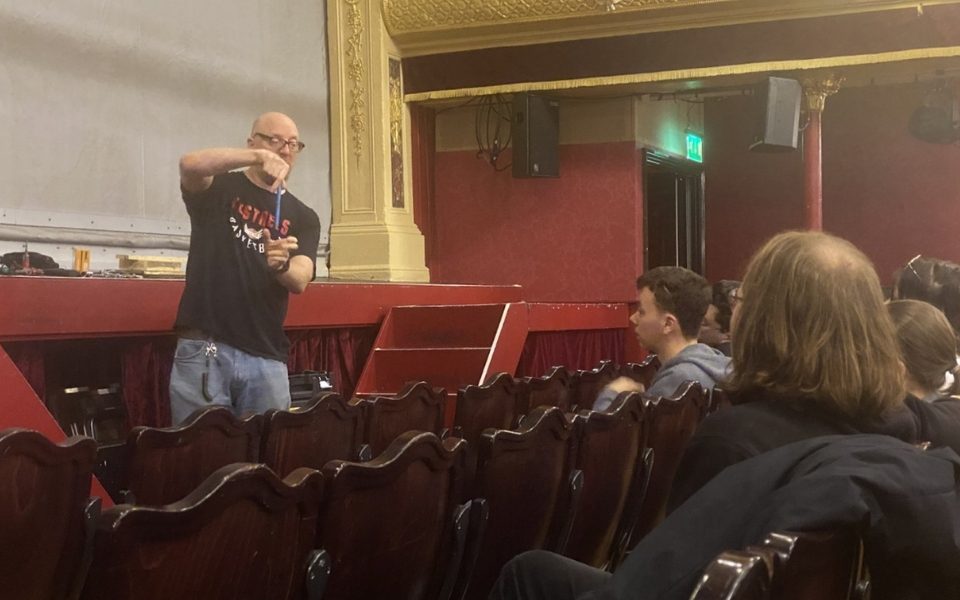 The Head of Stage standing in front of students seated in the City Varieties auditorium holding up a tool and giving a talk.