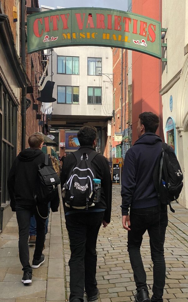Three students with their backs to the camera walking towards City Varieties under the green and red arched sign.
