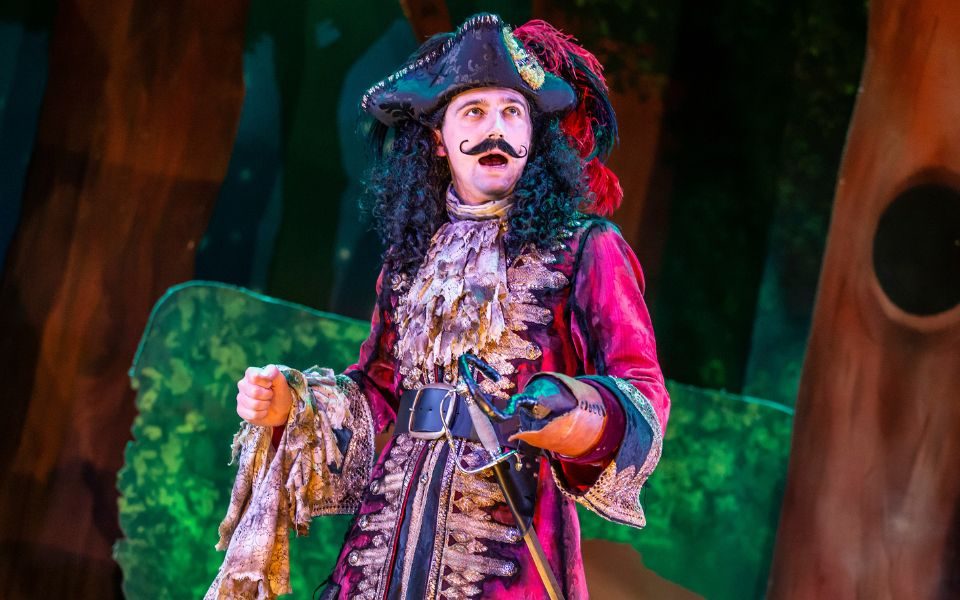 Captain Hook in Peter Pan Goes Wrong wearing a red pirate costume, giant moustache and hook for a hand