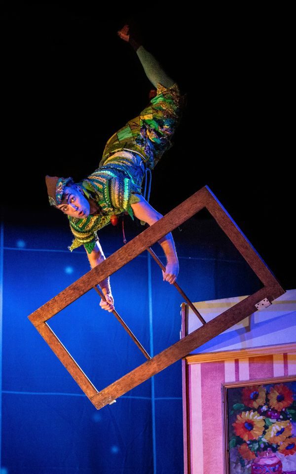 Peter Pan suspended in the air from wires holding up a large frame during Peter Pan Goes Wrong