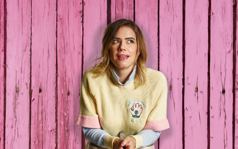 Lou Sanders leaning on some mannequin legs with pink wooden planks as the background.