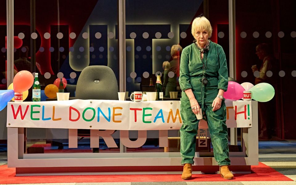 A woman in a green boiler suit leaning against a desk 'Well Done Team'.