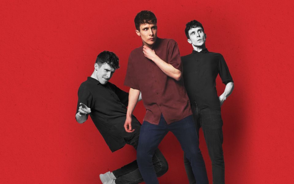 Promotional image featuring three versions of Larry, all doing different poses. The one in the front is in colour wearing a maroon shirt. The two behind are slightly smaller and are in black and white.