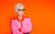 Jenny Eclair: Jokes Jokes Jokes Live! Jenny Eclair with her arms crossed wearing a pink and orange shirt and her signature black glasses against an orange background.