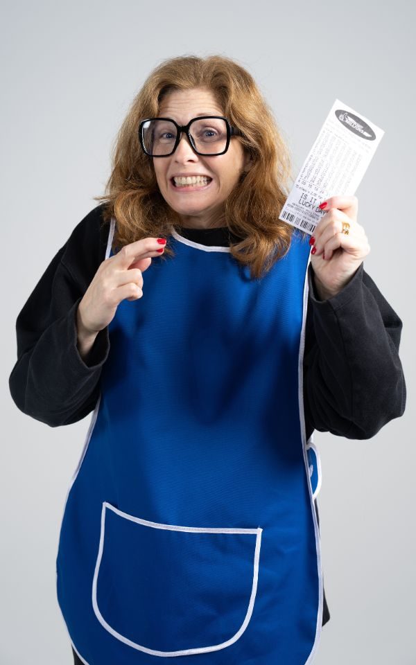 Samantha Giles crossing her fingers wearing big glasses and a blue tabard, and holding up a lottery ticket.