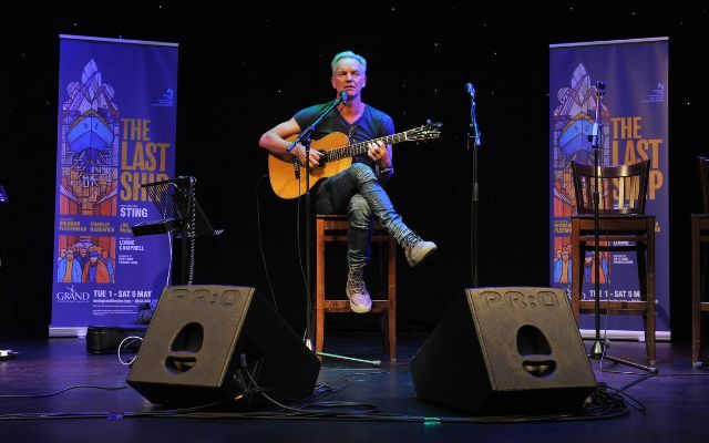 Sting sat on a stool at City Varieties playing guitar on stage in front of banners saying The Last Ship.