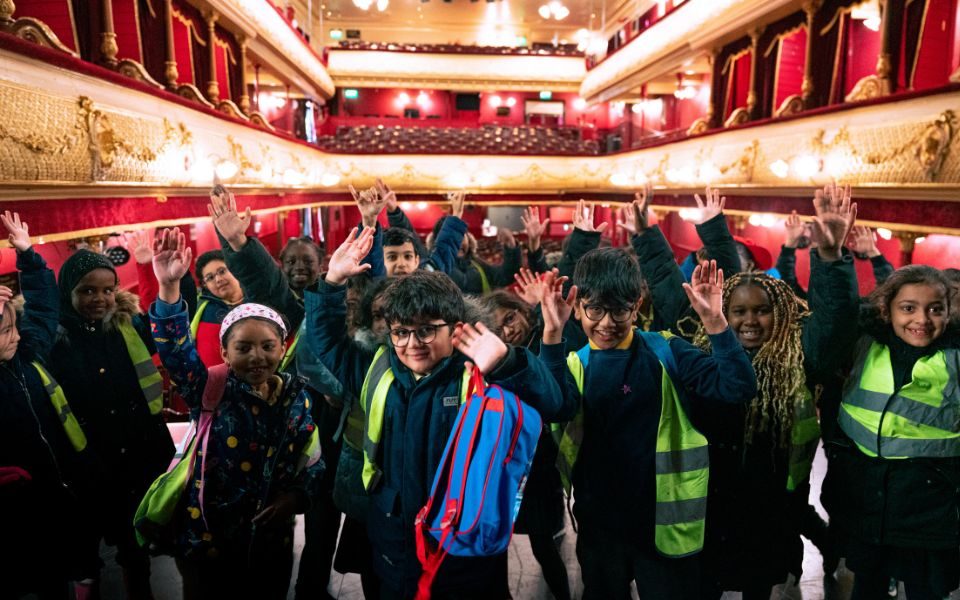 A group of primary schoolchildren in hi-vis pose on stage at City Varieties Music Hall with the auditorium in the background