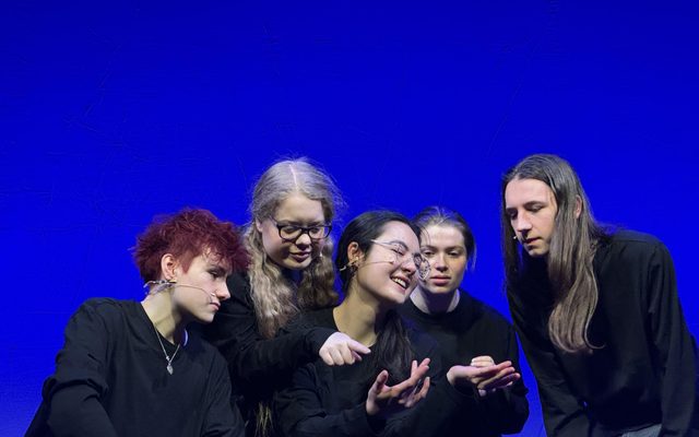 LAIT Holocaust Memorial Day Performance 2024 A group of actors dressed in black crowd around each other with their hands held out