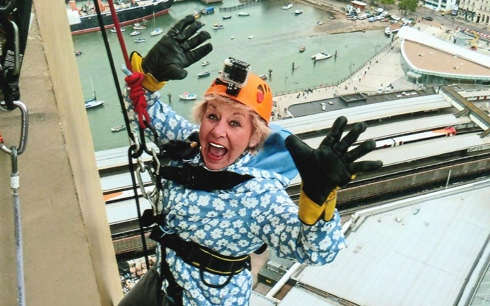 Jan Hunt smiling and holding her hands up while abseiling down a building.