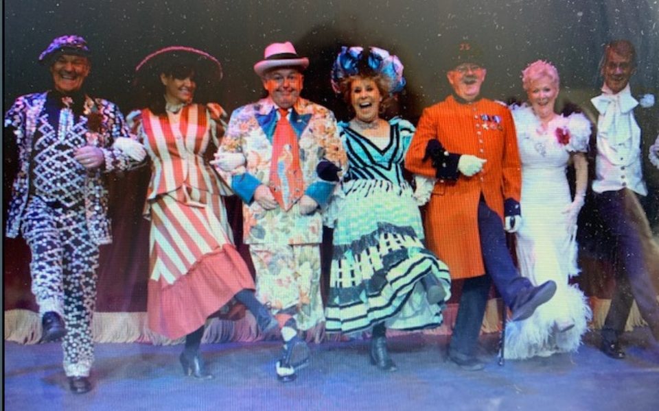 A row of people in colourful costumes linking arms and smiling for the camera.