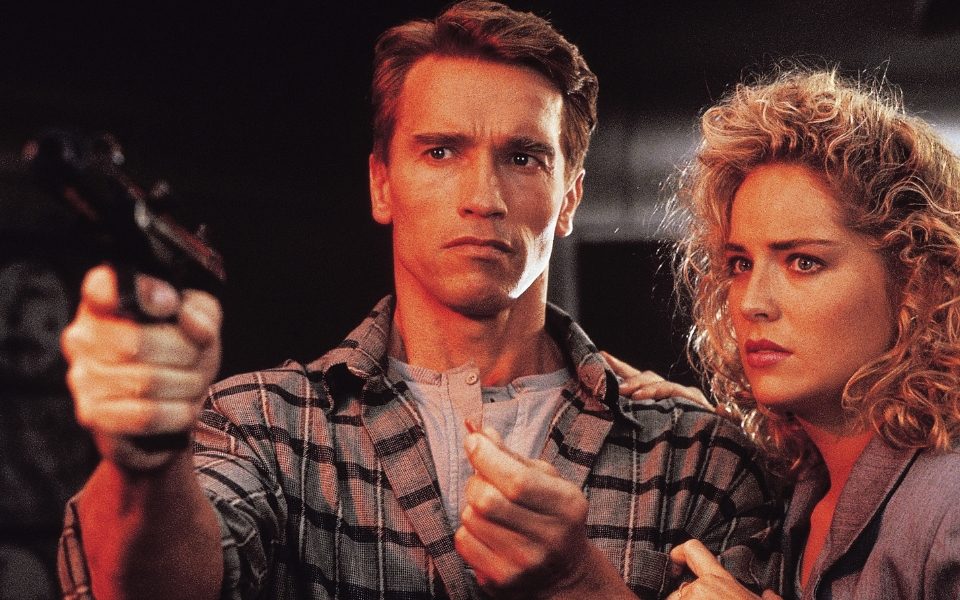 Arnold Schwarzenegger holding up a gun with Sharon Stone standing beside him in a scene from Total Recall (1990)