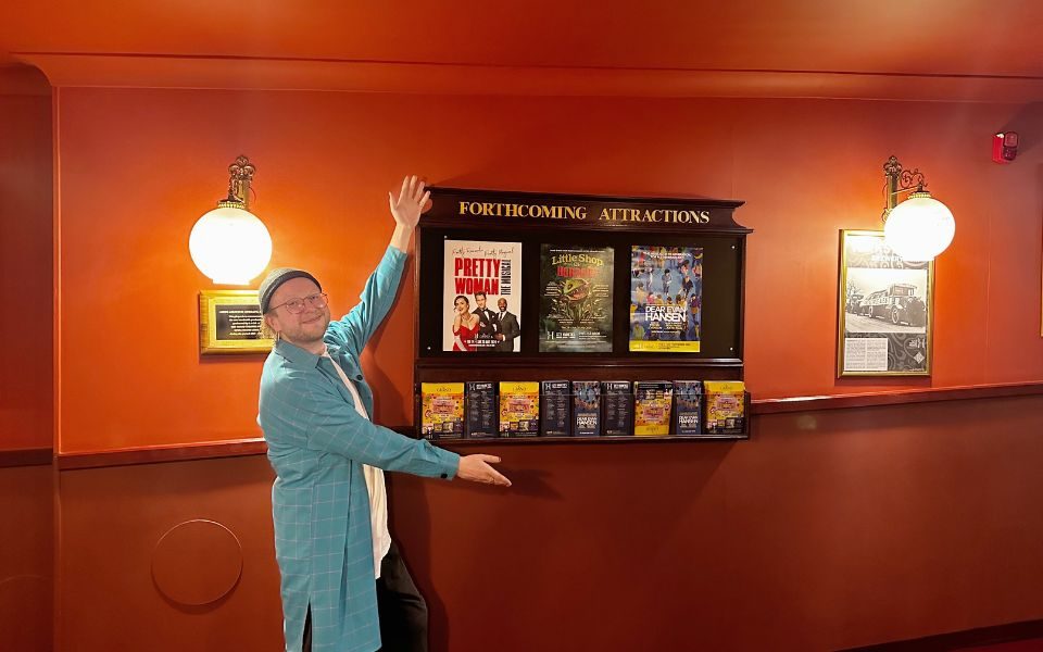 Henry poses showing a poster board advertising upcoming shows.