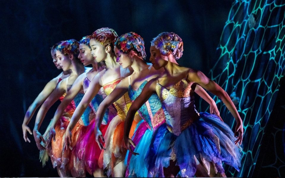 Dancers in colourful costumes standing in the same pose in a row.