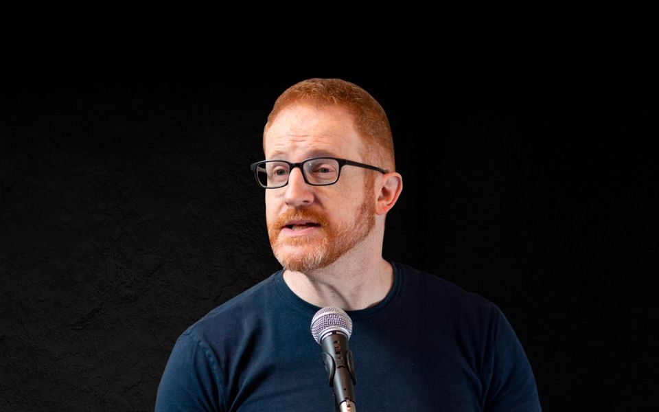 Steve Hofstetter holding a microphone against a black background.