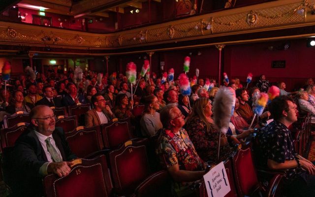 An audience at City Varieties Music Hall holding colourful feather dusters.