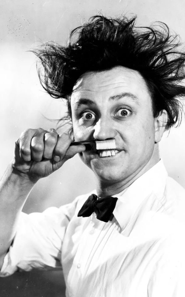 Sir Ken Dodd poses with a toothbrush held to mimic a moustache