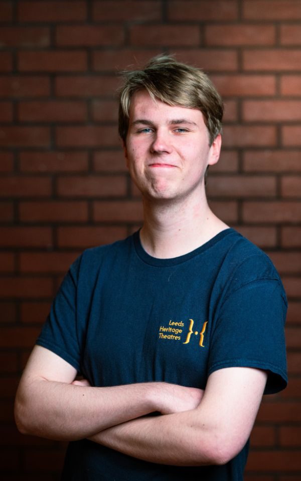 A young actor in his youth theatre t-shirt poses for a headshot with his arms folded