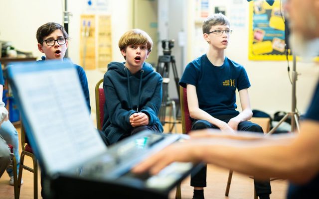 A group of three young actors during a singing session with a keyboard in the front of frame