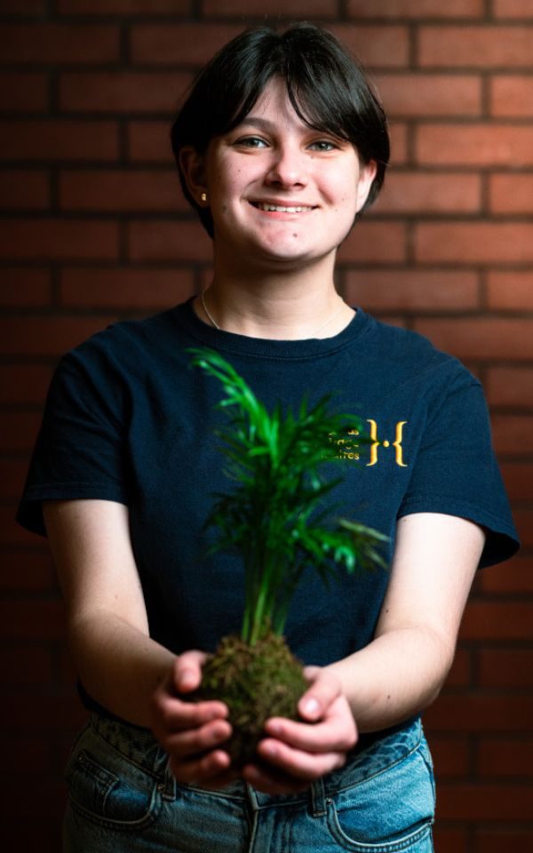 A young actor in a youth theatre t-shirt holds a little plant posing as Seymour from Little Shop of Horrors.