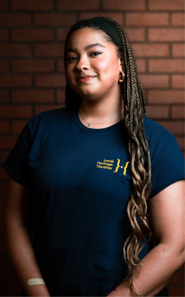 An actor with long braided hair poses for a headshot in her youth theatre t-shirt