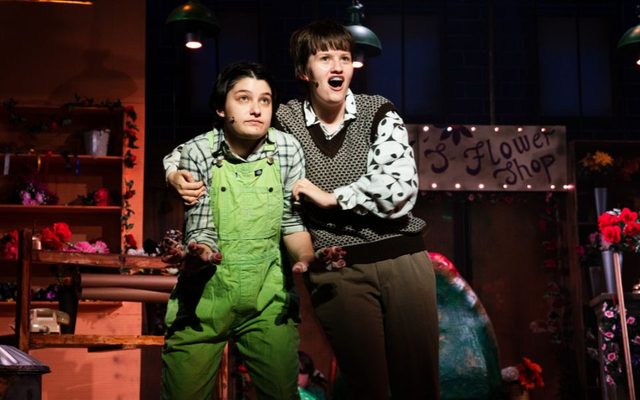 Seymour and Mushnik. Credit Chris Coote A young actor in green dungarees looks concerned, as another actor in retro costume pulls them close while singing