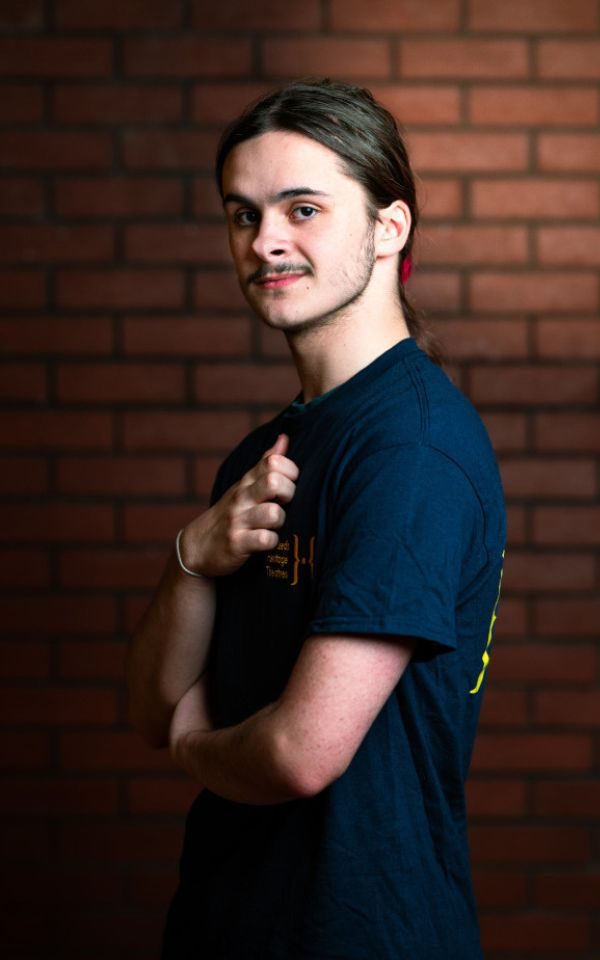 A young actor in their youth theatre t-shirt poses for a headshot turning to the side with hand on their chest