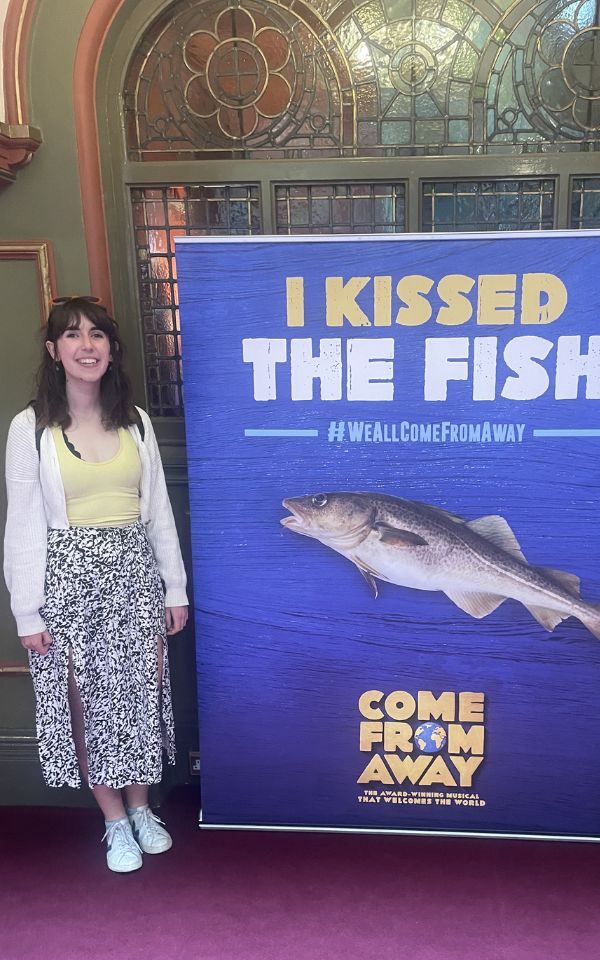 Sarah stood smiling next to a sign reading 'I Kissed The Fish' with an image of a fish