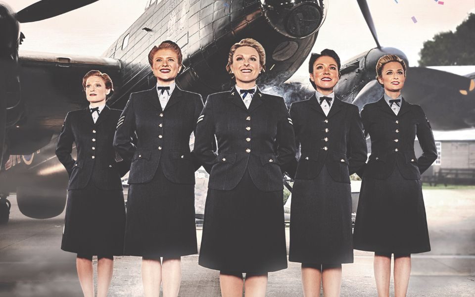 Five women in war-time military dress with their hands behind their backs stood in front of a fighter jet. Bunting appears at the top.