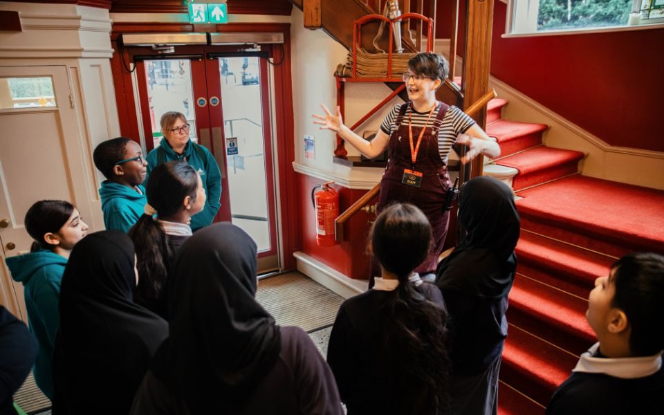 Sylvia Barber stands on the stairs in the HPPH foyer and talks animatedly to a group of school children.