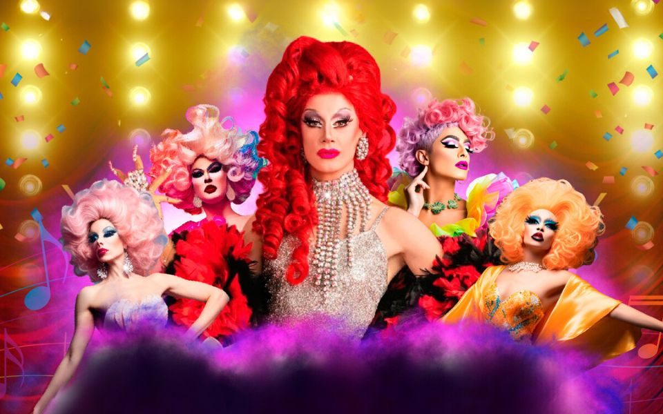 Divina De Campo with her signature red hair wearing silver surrounded by four other Drag artists and confetti.