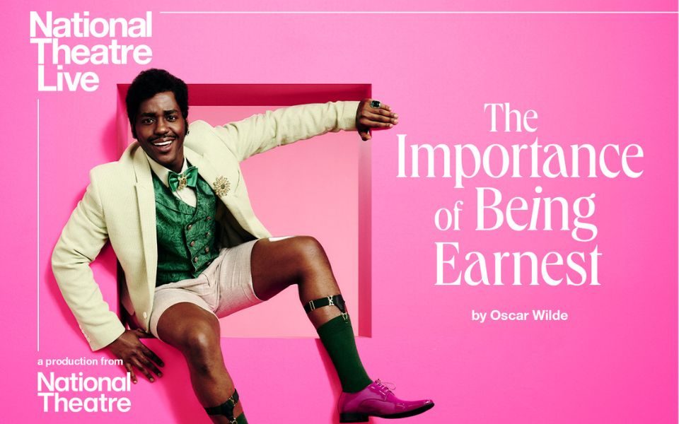 Ncuti Gatwa wearing a suit jacket, waist coat, bow tie and shorts sat in a cut out in a pink wall. Text reads National Theatre Live. A production from National Theatre. The Importance of Being Earnest by Oscar Wild.