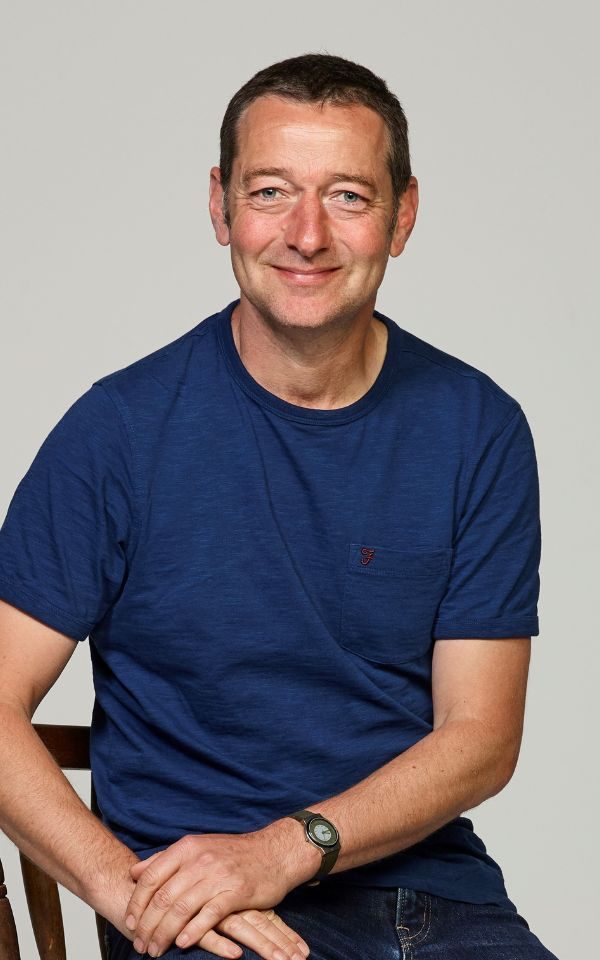 Ned boulting wearing a navy t-shirt sat down and smiling.