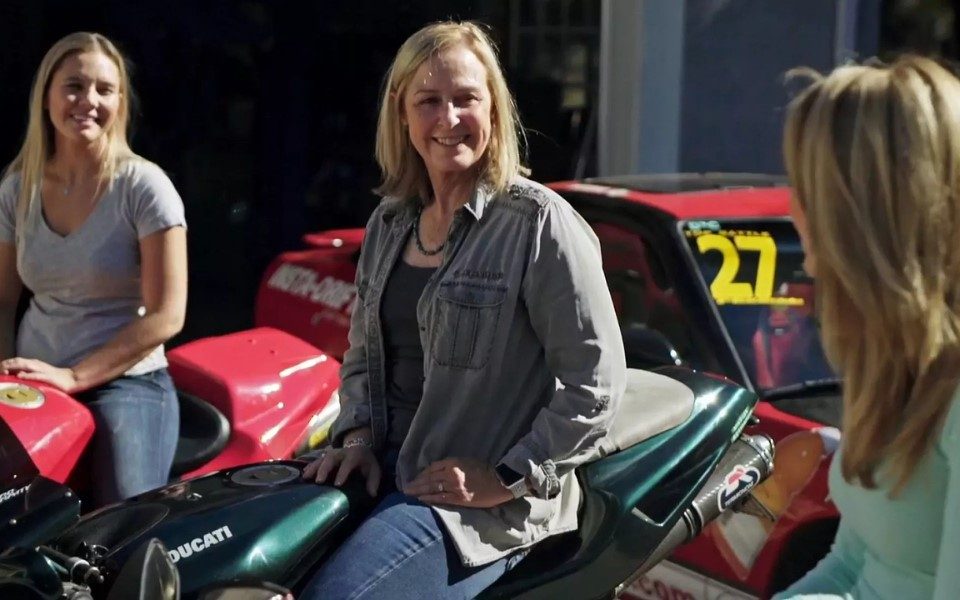 Two stunt artists sat on two stunt vehicles. Both are smiling at another person facing away from the camera. All are wearing casual clothing including jeans.