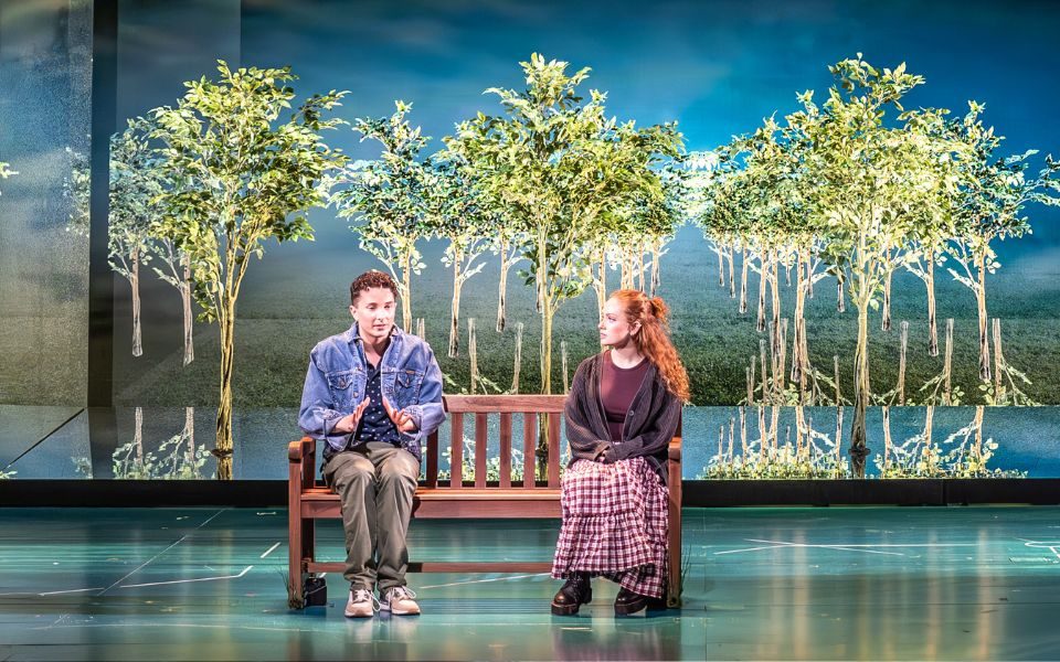 Ryan Kopel (Evan Hansen) and Lauren Conroy (Zoe Murphy) sat on a bench with projections of trees around them.