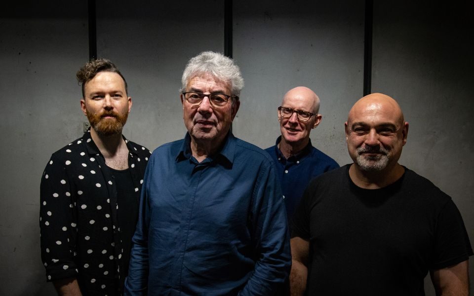 Graham Gouldman and the three other members of Heart Full of Songs smiling at the camera wearing either navy or black on the top.