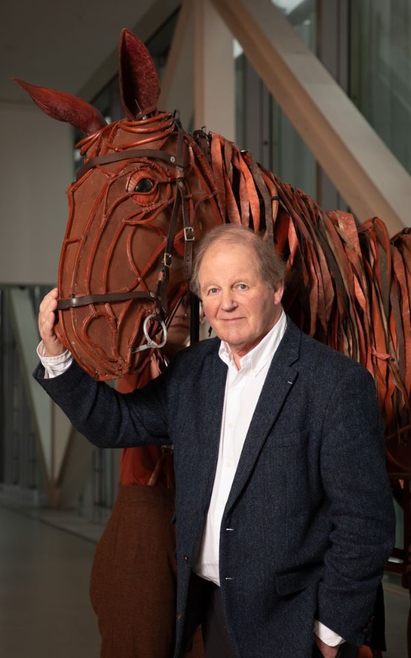 Michael Morpurgo with his hand on Joey (a lifesize horse puppet)'s head.