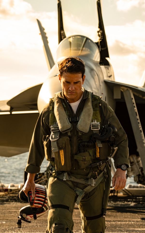 Tom Cruise as Maverick in military uniform looking down with a military plane blurred in the background.